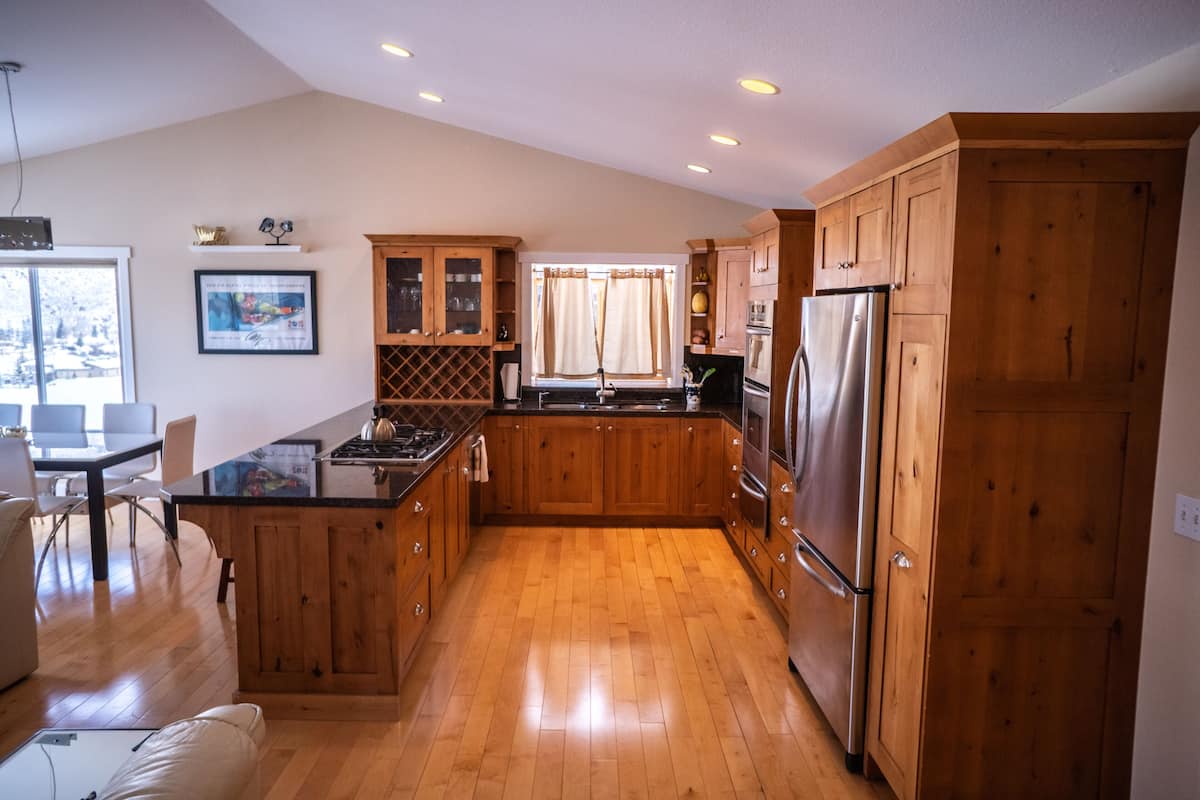 Una cocina con armarios de madera, un refrigerador de acero inoxidable y un comedor con mesa y sillas.