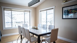Un comedor con una gran mesa, seis sillas y vistas a montañas nevadas a través de amplios ventanales.