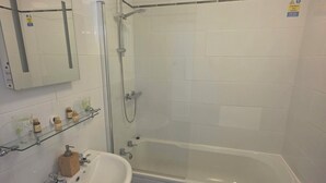 Un baño moderno con ducha de vidrio, lavamanos blanco y dispensador de jabón de madera, y un inodoro.