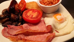 Un plato de comida para el desayuno con tocino, huevos, champiñones, tomates y frijoles horneados.