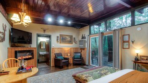 A cozy room with a fireplace, a television, a large window with a forest view, and a bed with a patterned bedspread.