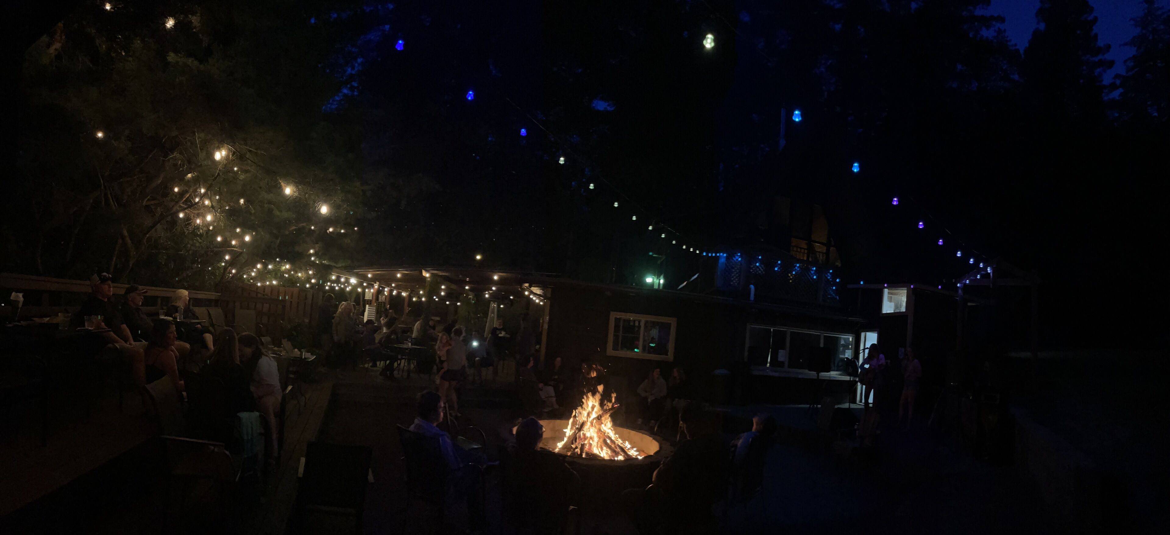 Un área de comedor al aire libre con luces colgantes y una chimenea.