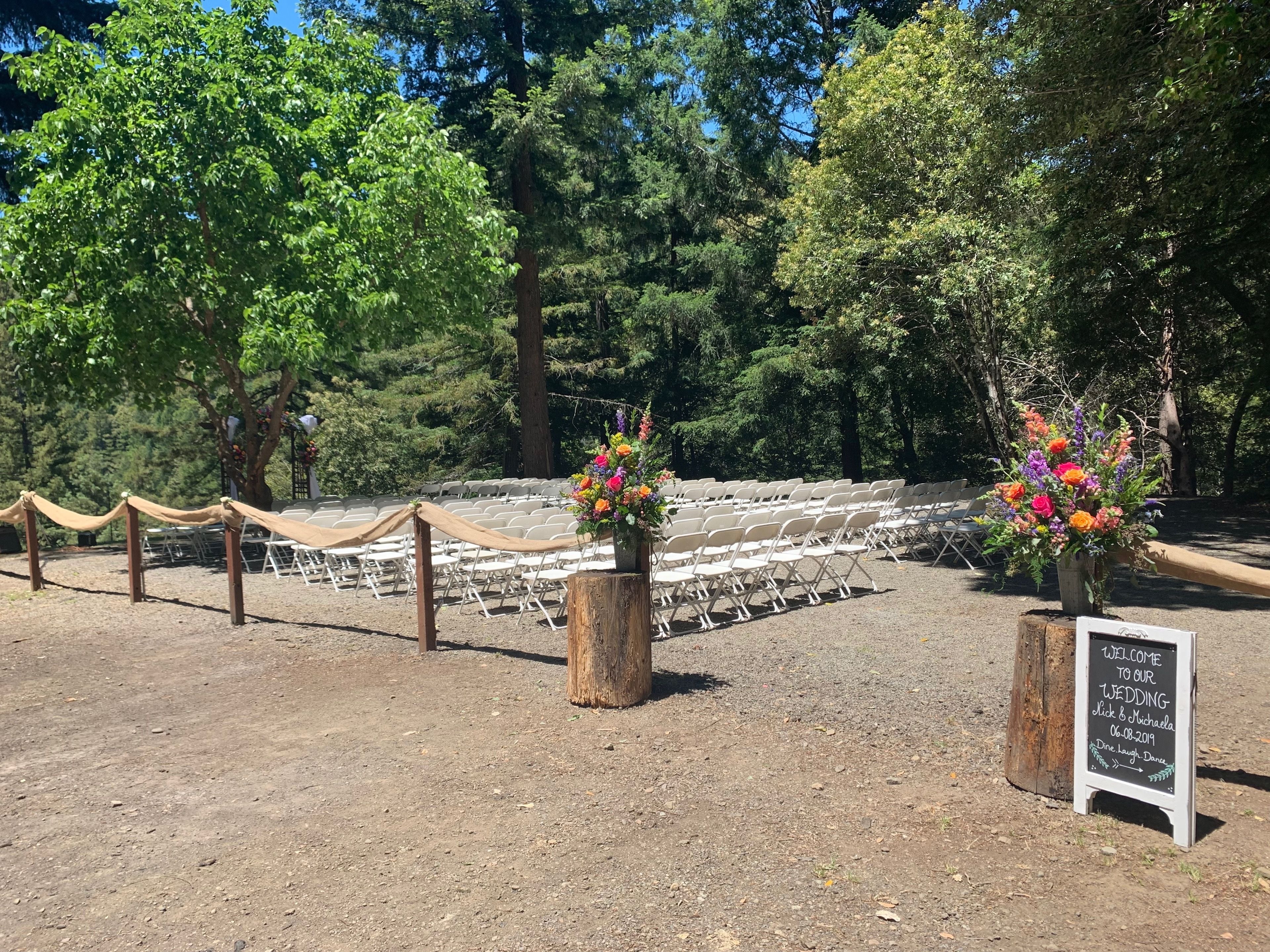 An outdoor wedding venue with rows of white chairs, a wooden fence, and a welcome sign.