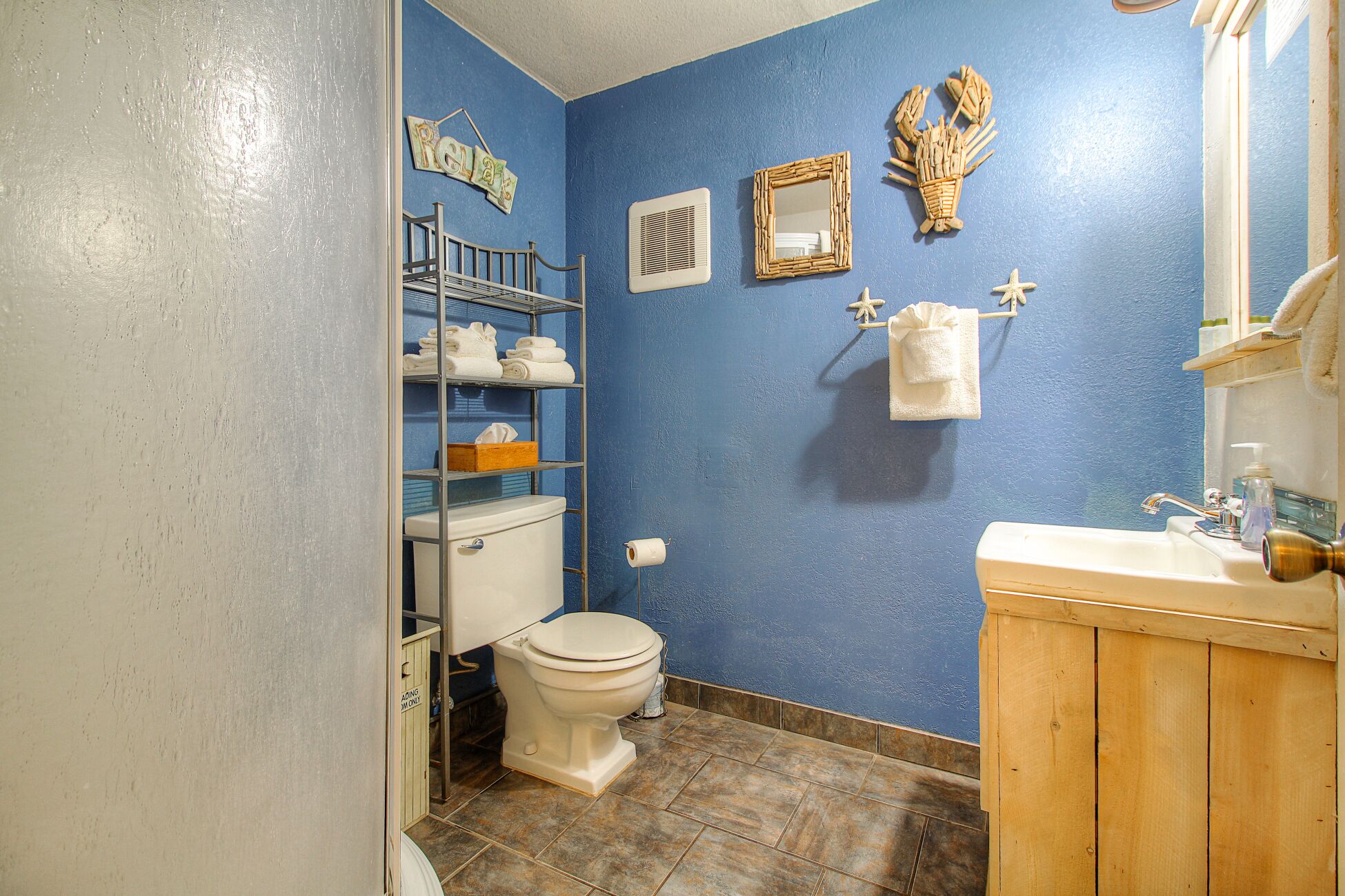Een badkamer met een blauwe wand, een wit toilet, een houten kastje, een plank met handdoeken, een spiegel en een handdoekhouder.