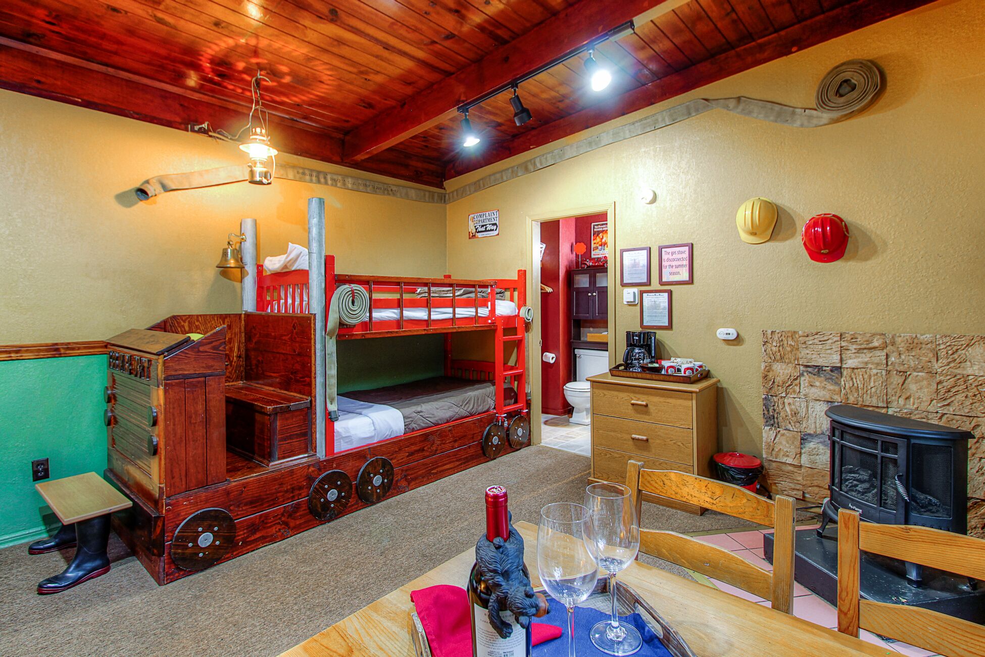 A cozy room with a bunk bed, a wooden desk, a fireplace, and a dining area with wine glasses.