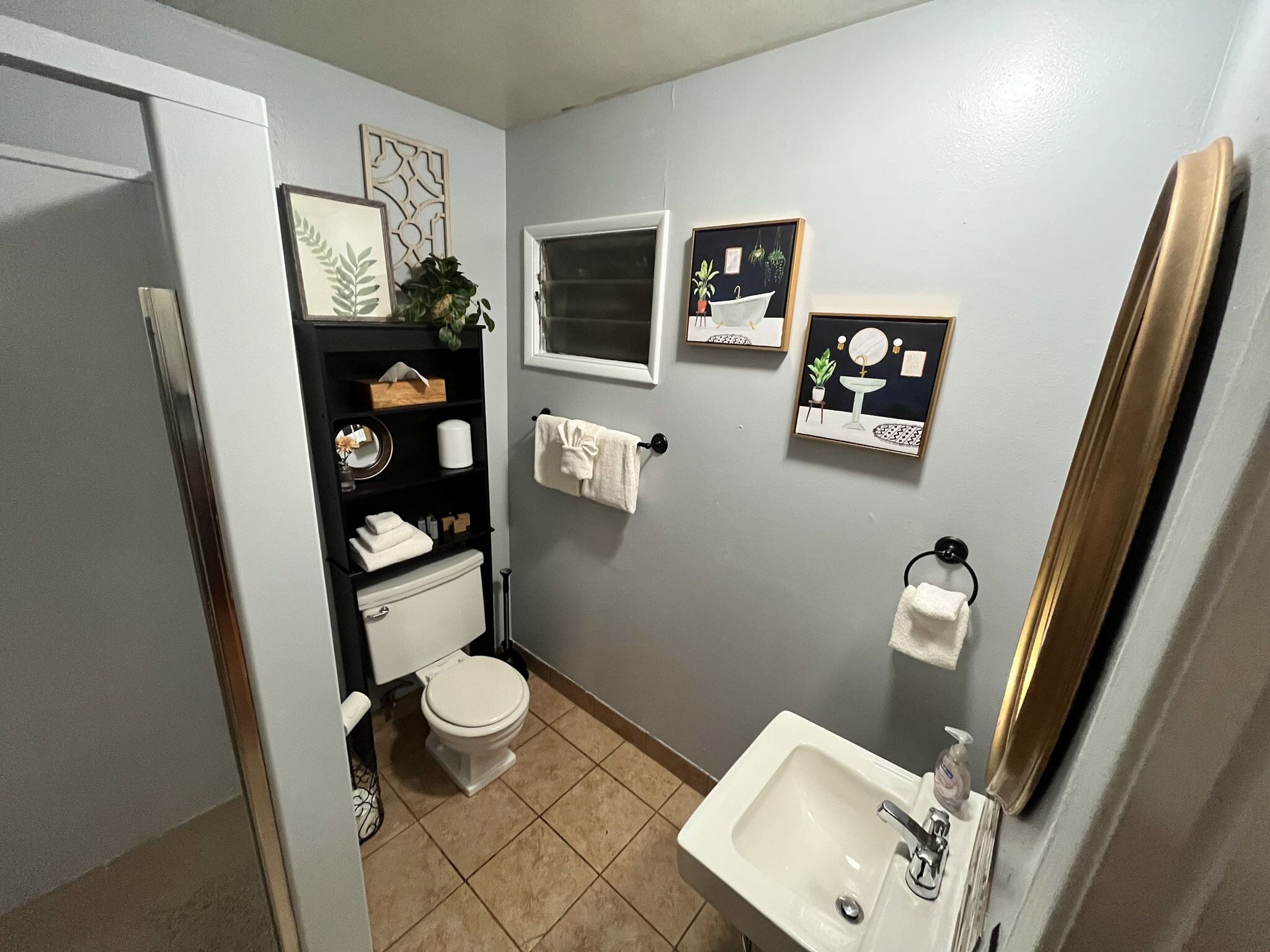 A compact bathroom with a toilet, sink, and shelves with toiletries.