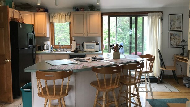 A kitchen with a central island, wooden chairs, a refrigerator, a microwave, and a window with curtains. -  Charming 2 bedroom rental Pond Village area available  June 8-17 (north truro)