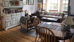 A cozy living room with a sofa, chairs, a coffee table, and a bookshelf filled with books and decorative items. -  Charming 2 bedroom rental Pond Village area available  June 8-17 (north truro)