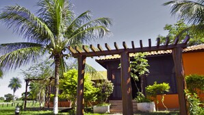 A wooden pergola with a thatched roof, surrounded by lush greenery and palm trees. - Pantanal Ranch Meia Lua (Miranda)
