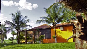 A house with a yellow exterior, surrounded by a well-maintained lawn and palm trees. - Pantanal Ranch Meia Lua (Miranda)