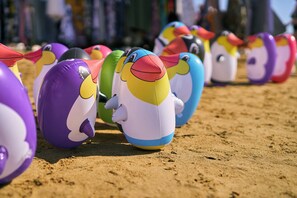 A row of colorful beach balls shaped like penguins on a sandy surface.