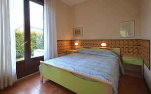 A bedroom with a bed, bedside tables, and a view through a glass door. - Holiday apartment with terrace (Bibione)