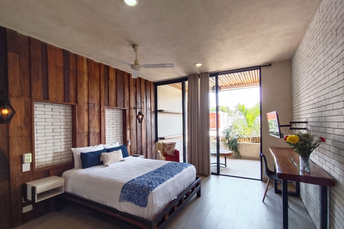 A modern bedroom with a large bed, a desk, and a view of the outdoors.