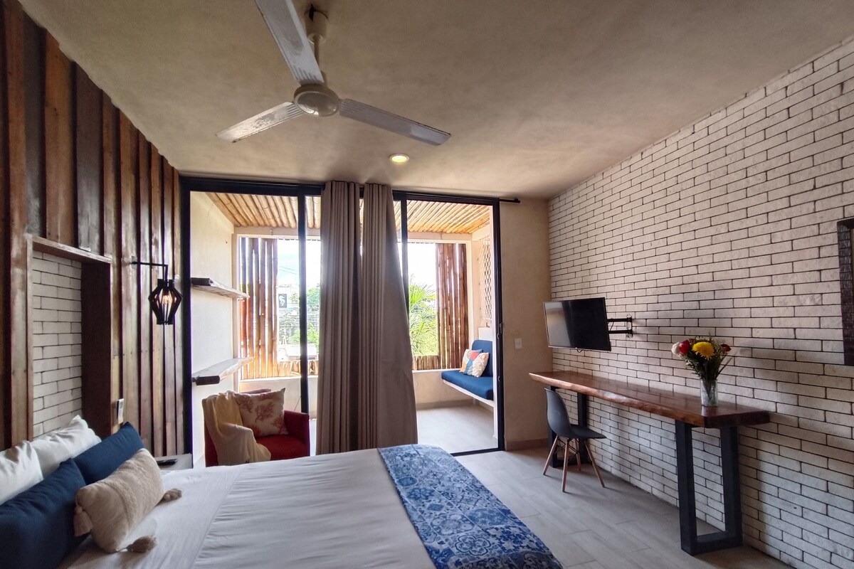A modern hotel room with a large bed, a desk with a flat-screen TV, and a balcony with a view.