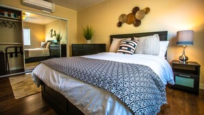 Un dormitorio con cama, mesitas de noche, lámpara, espejo y ventilador de techo.