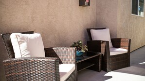 Un patio con mobiliario de mimbre, una pequeña mesa y una planta en maceta.