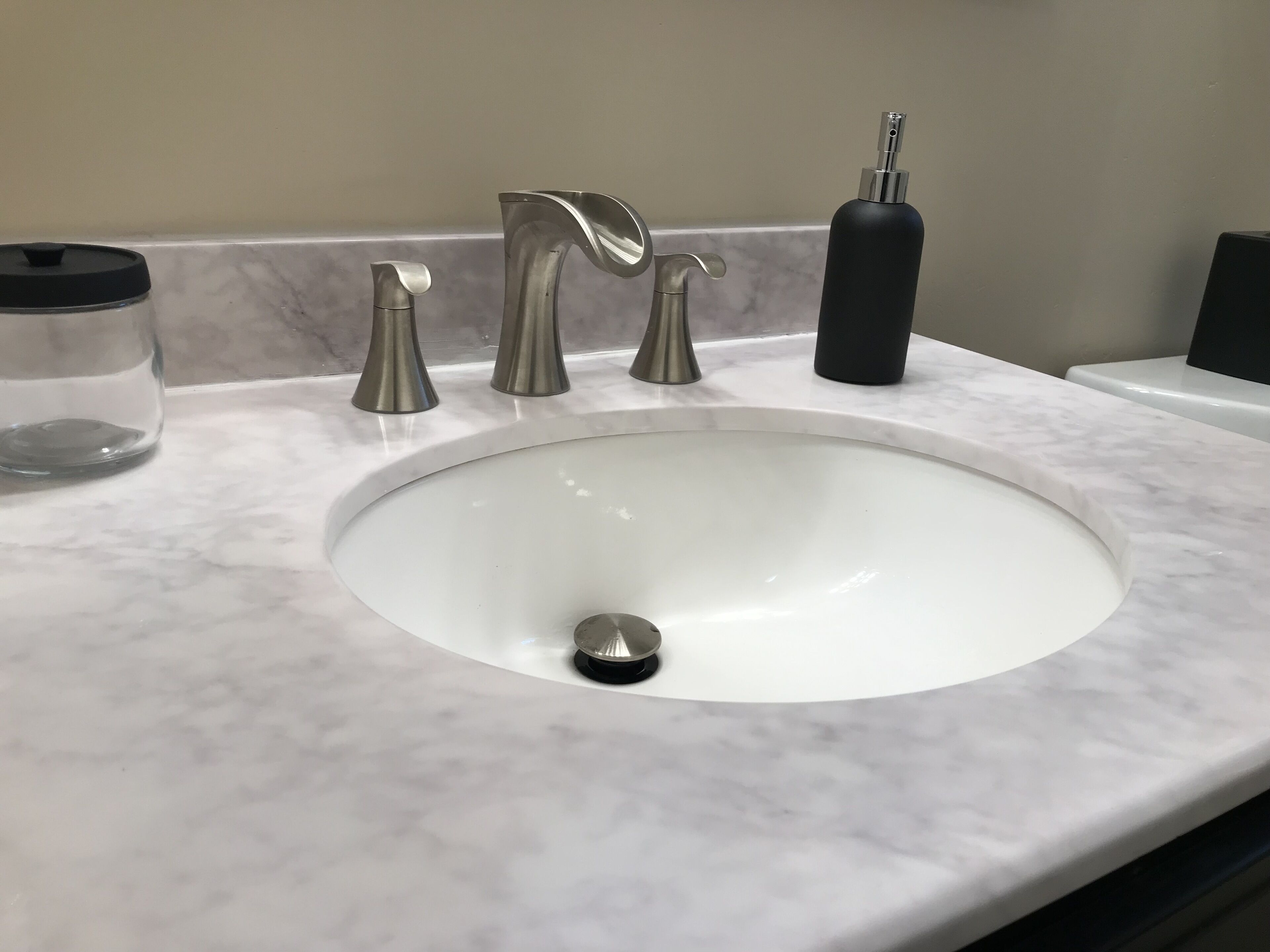 A bathroom sink with a marble countertop, a faucet, and a soap dispenser.