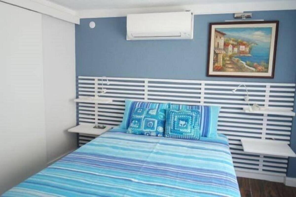 A bedroom with a bed, white headboard, and a painting on the wall.