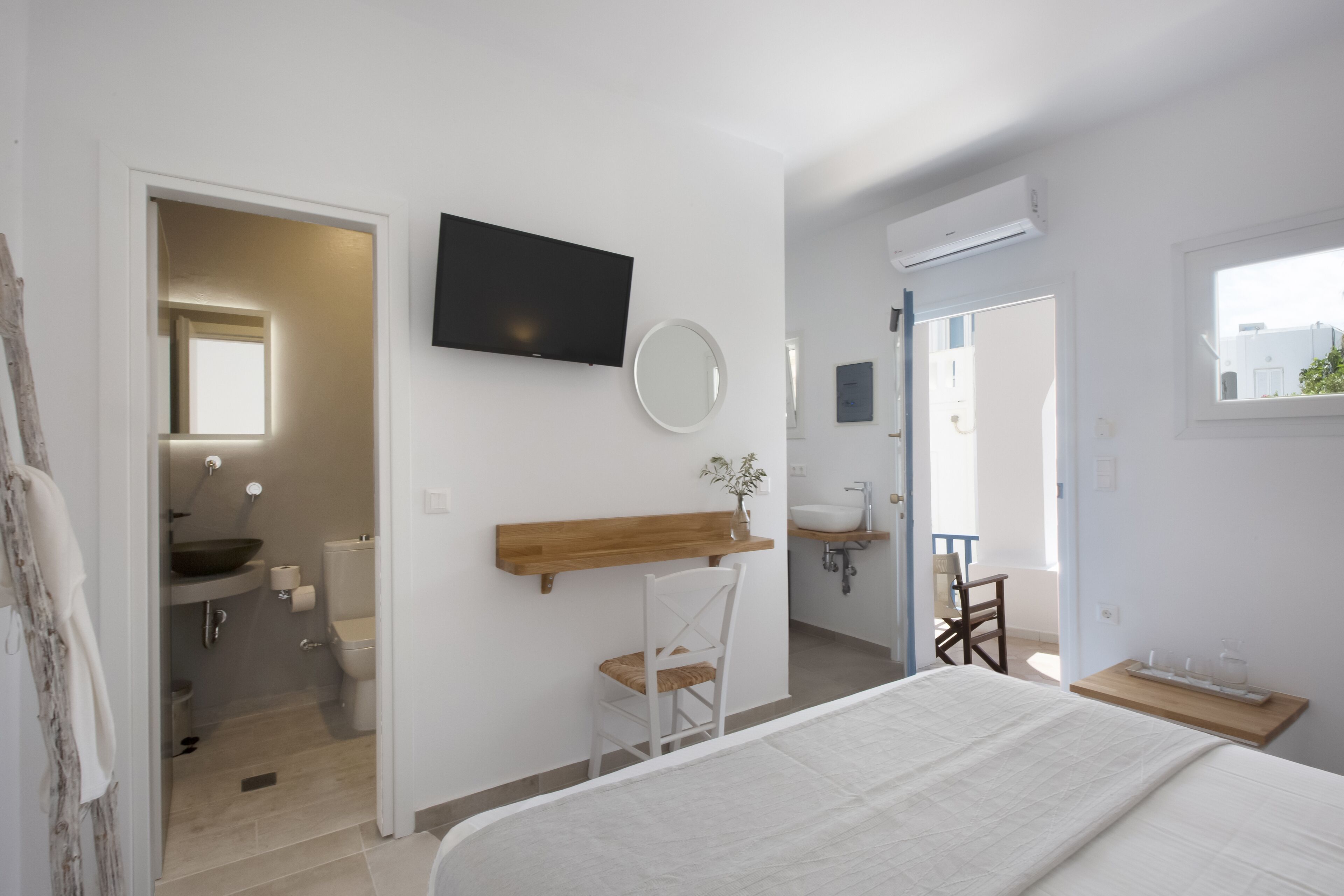 A bedroom with a bed, a TV mounted on the wall, a wooden shelf, a chair, and a window.