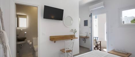 A bedroom with a bed, a TV mounted on the wall, a wooden shelf, a chair, and a window.
