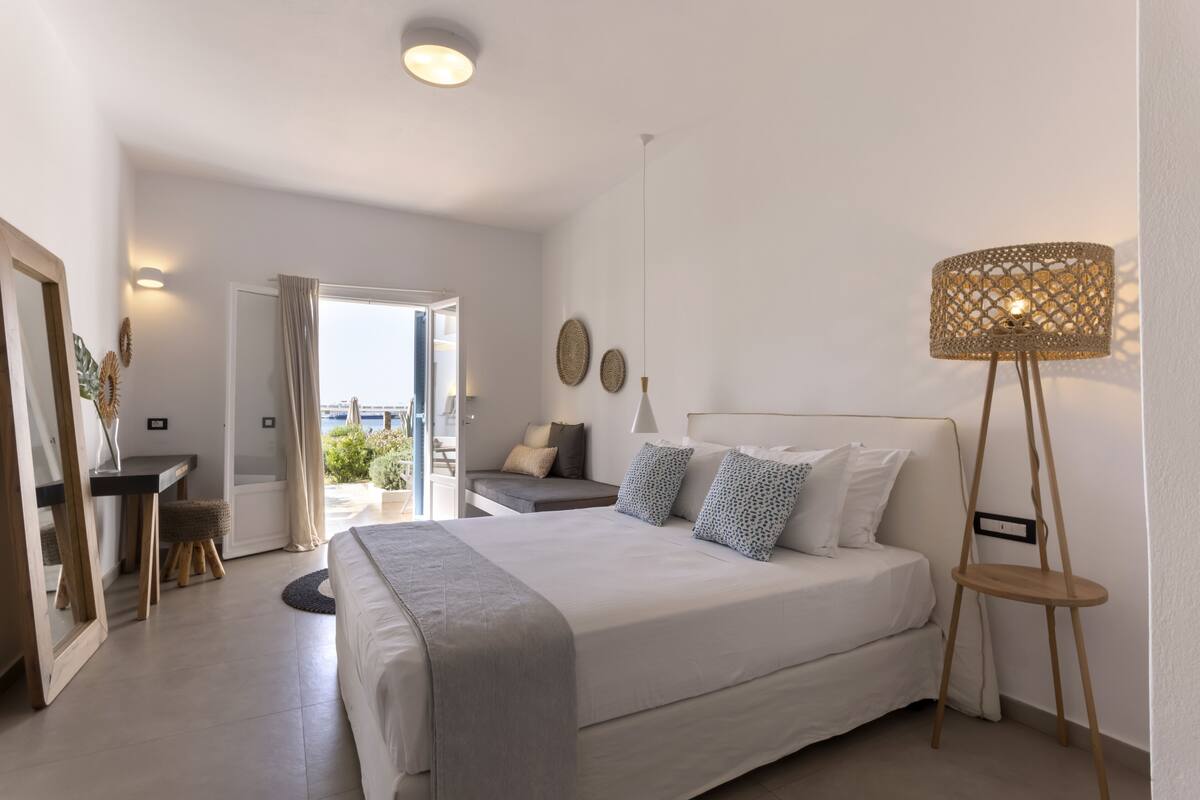 A modern bedroom with a large bed, a desk, and a view of the outdoors.