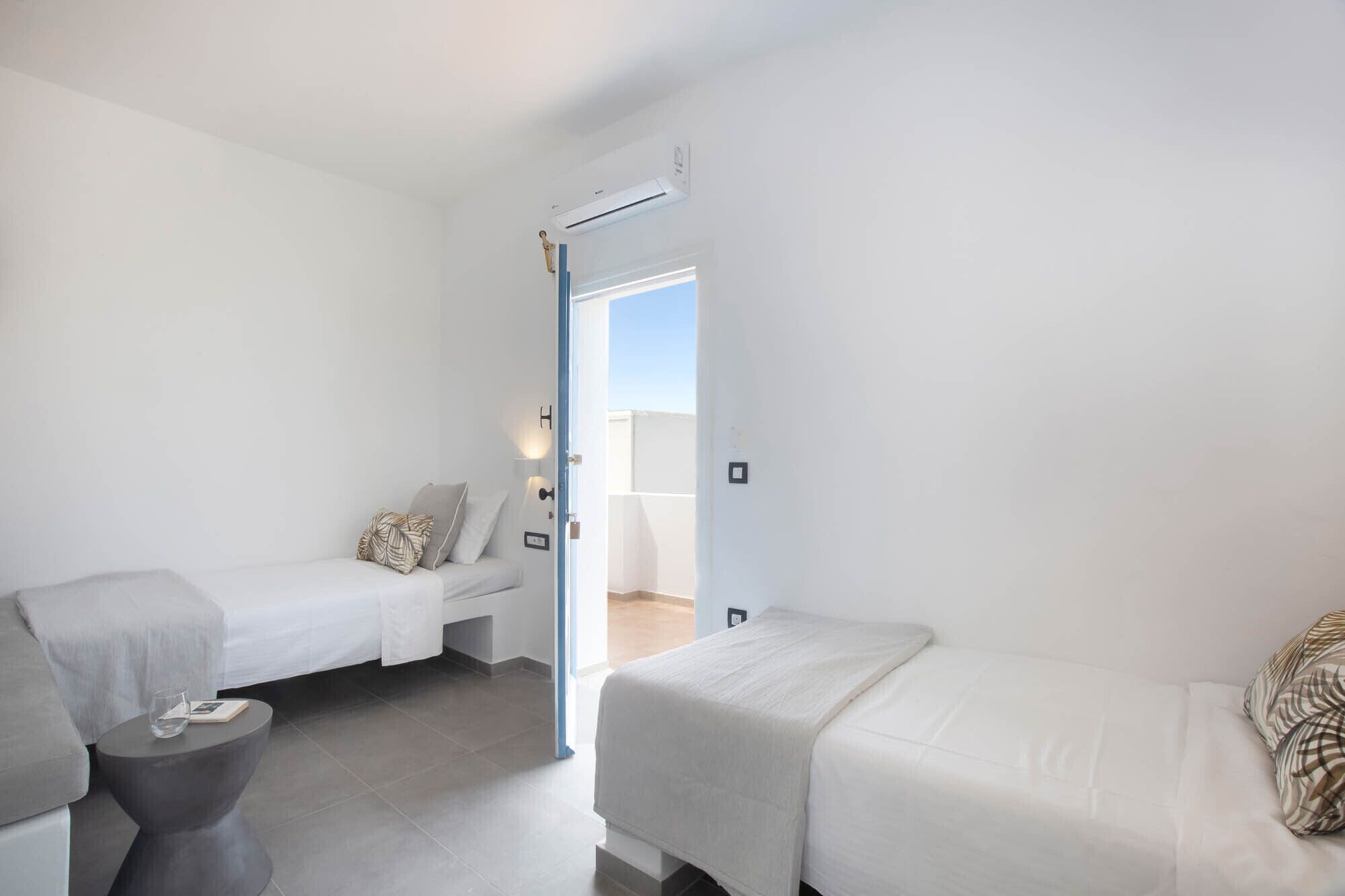 Una camera da letto con due letti singoli, un tavolino rotondo con un bicchiere e un libro, e una porta che dà su un balcone.