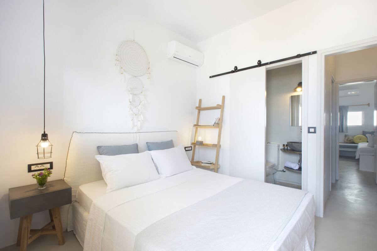 A bedroom with a bed, bedside table, wall-mounted air conditioner, and a ladder against the wall.