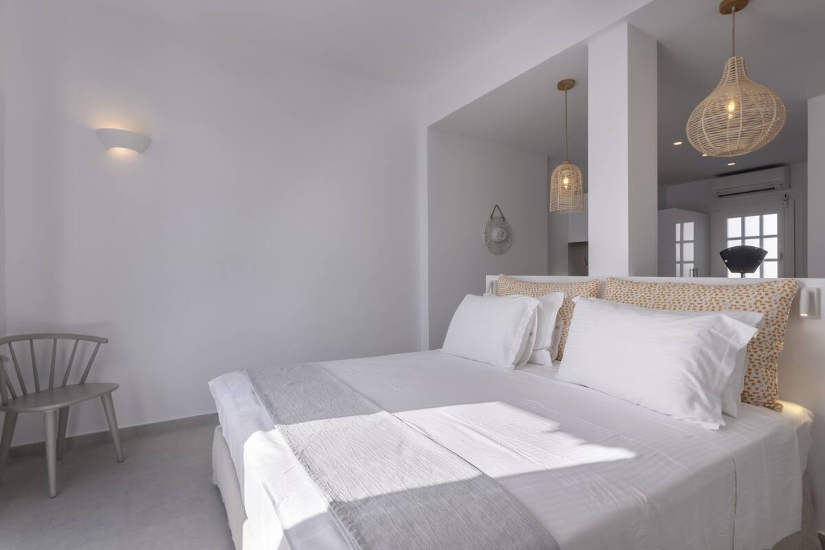 A bedroom with a large bed, a chair, and a hanging light fixture.