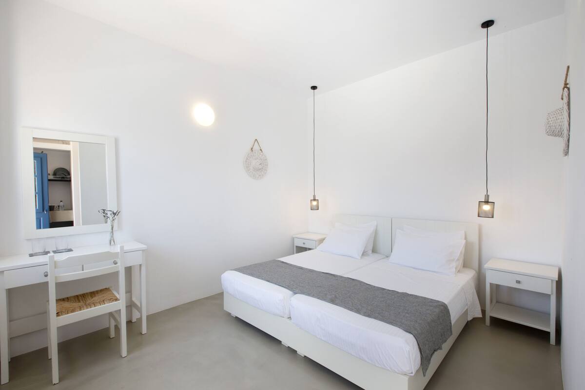 A minimalist bedroom with a white bed, bedside tables, a desk, and a mirror.
