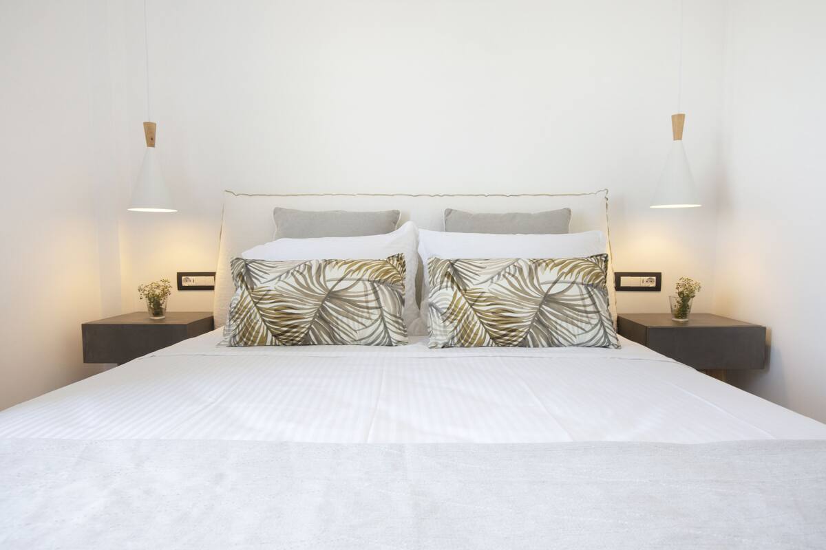 A neatly made bed with a white duvet and patterned pillows, flanked by two bedside tables with lamps and small vases.