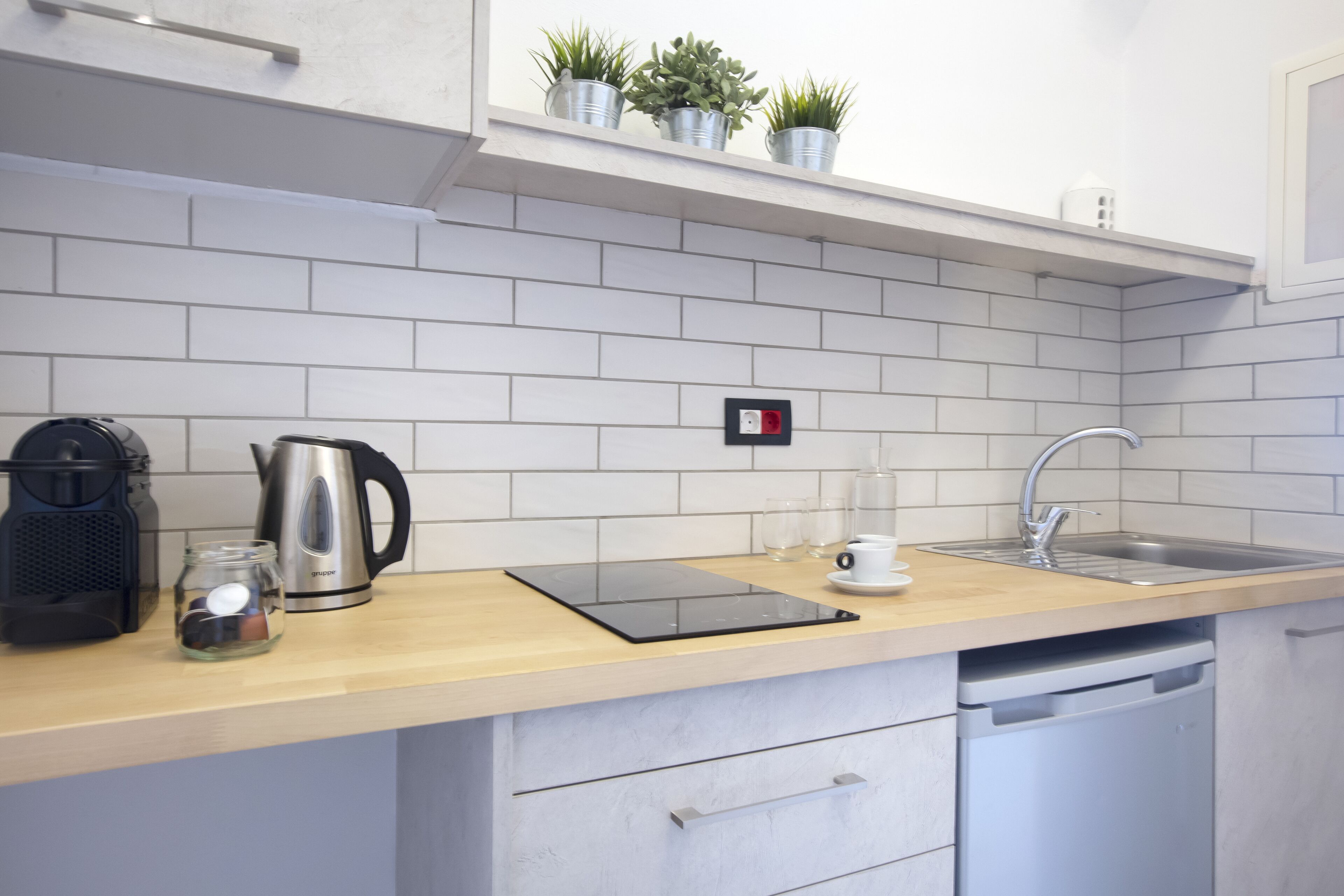 Une cuisine moderne avec des carreaux blancs, un plan de travail en bois, une machine à café, une bouilloire, un évier et un lave-vaisselle.