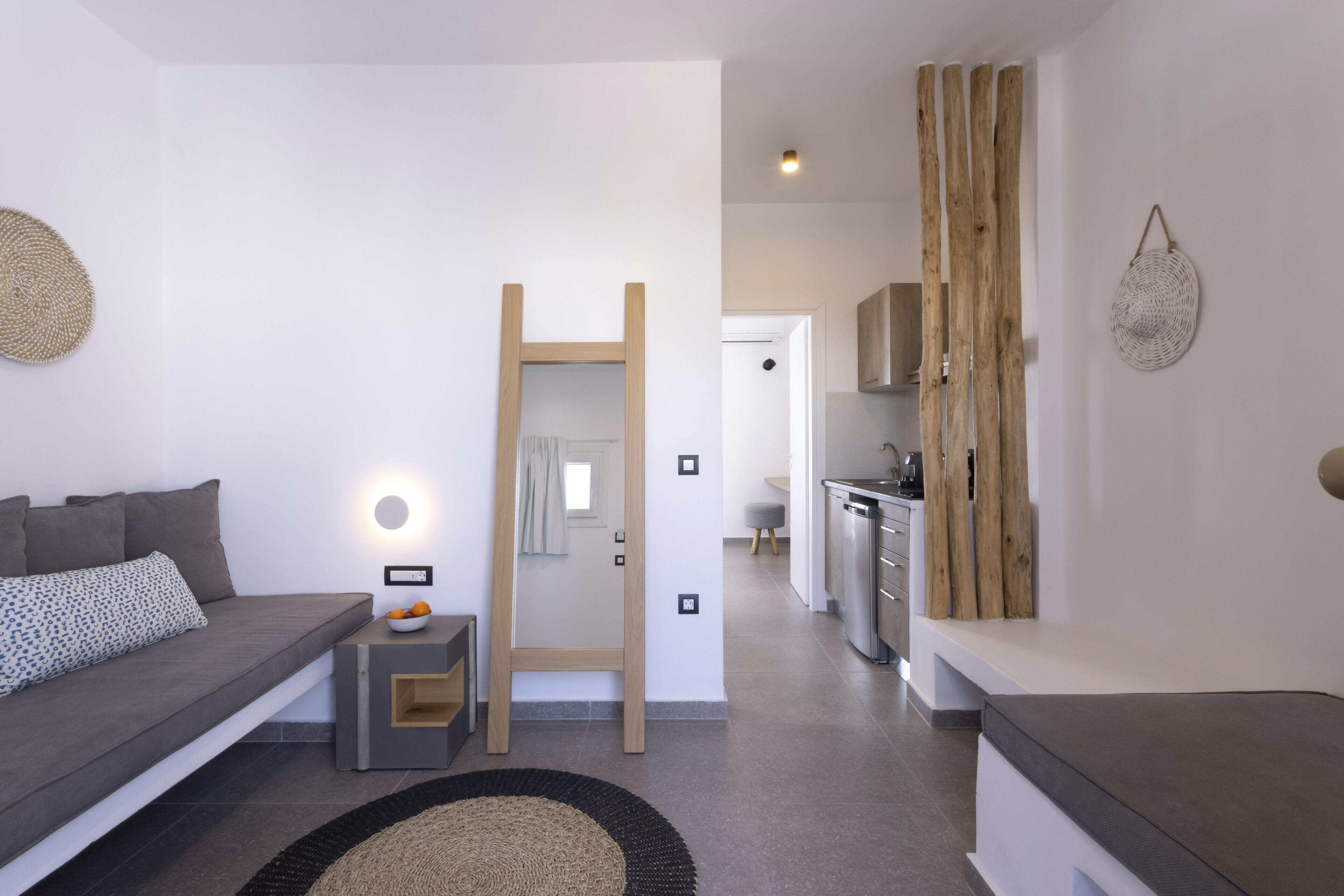 Un salon moderne avec un canapé gris, une petite table d’appoint, une échelle en bois et, au fond, un coin cuisine.
