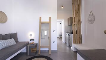 Un salon moderne avec un canapé gris, une petite table d’appoint, une échelle en bois et, au fond, un coin cuisine.