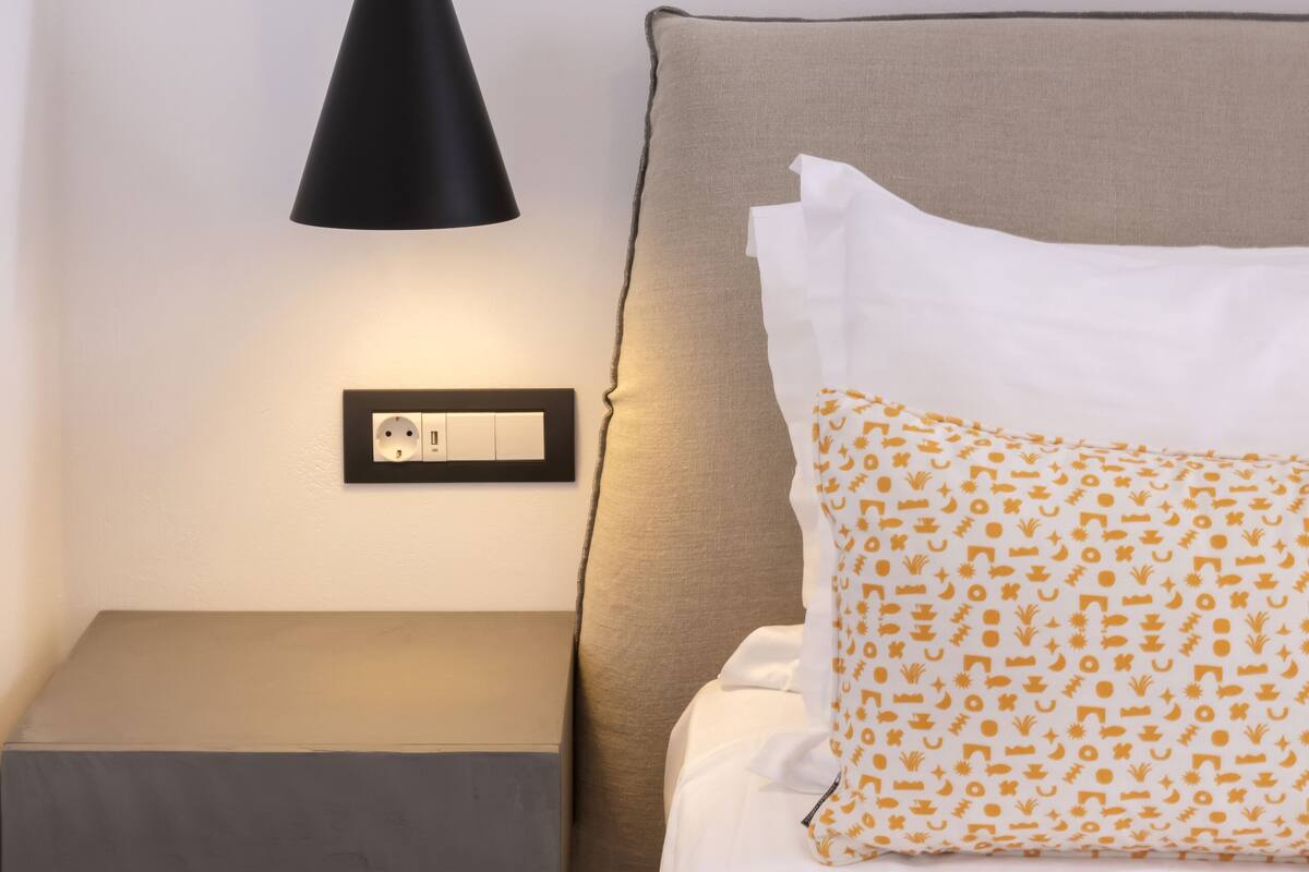 A bed with a patterned pillow, a bedside table, and a black pendant light.