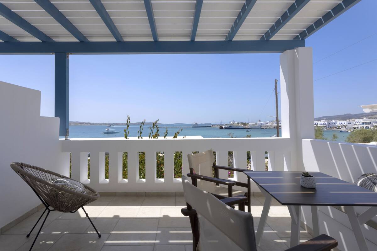 A balcony with a view of the sea, a table, and two chairs.