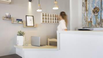 Un área de recepción con un mostrador blanco, una computadora portátil, un certificado enmarcado y una estantería con fotos enmarcadas.