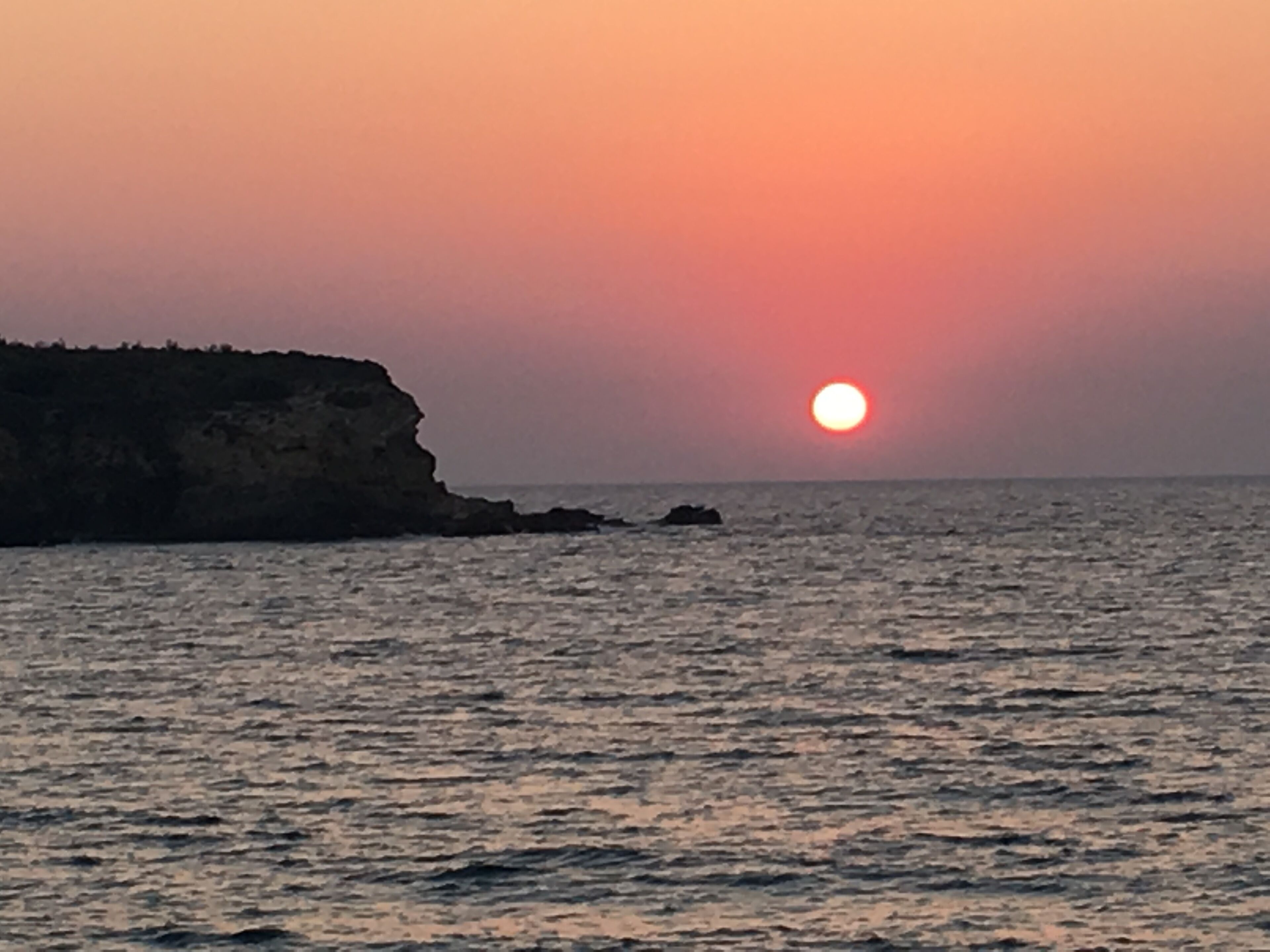 Un atardecer sobre el océano con un litoral rocoso.