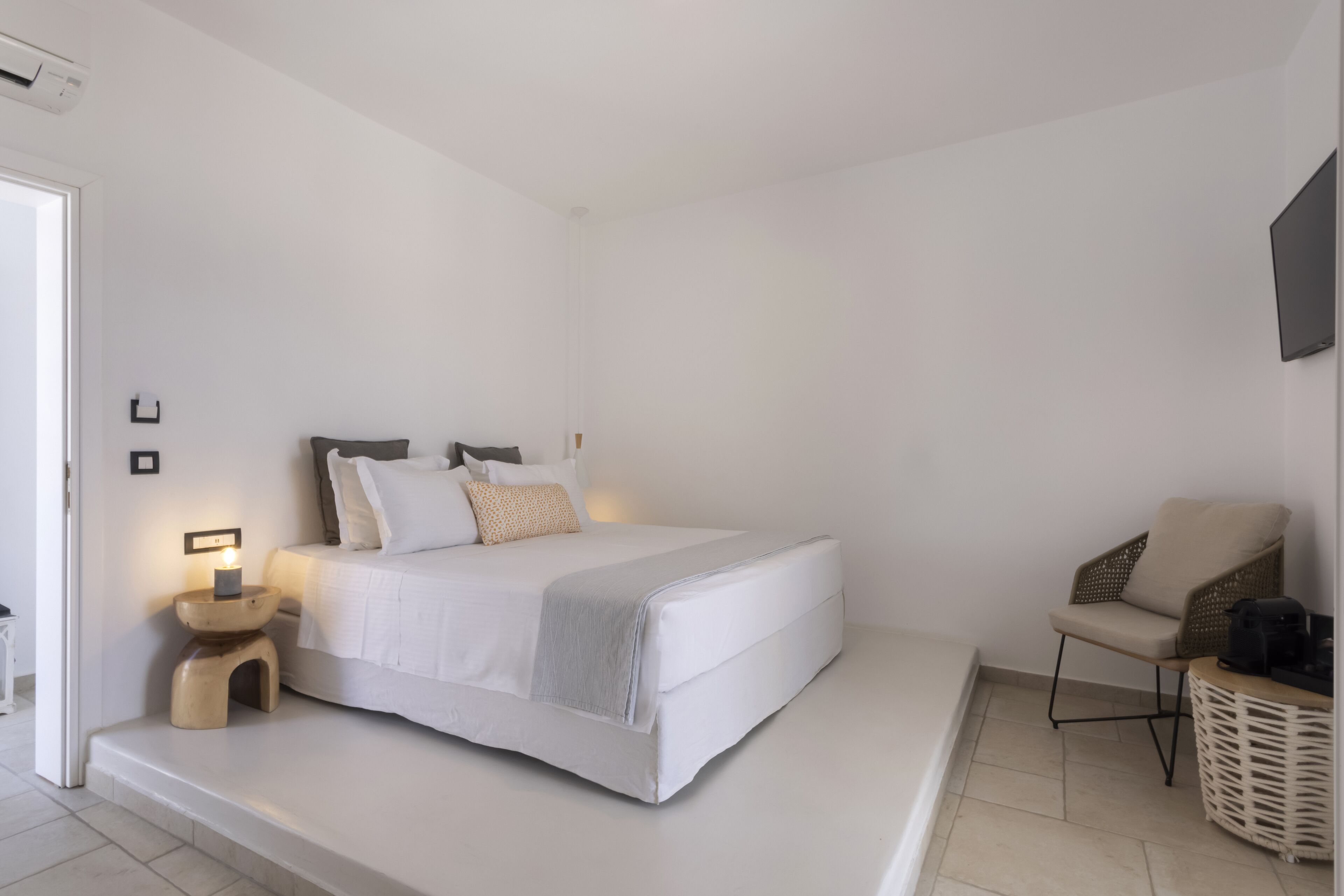 Un dormitorio minimalista con cama, mesita de noche, silla y televisor montado en la pared.