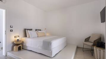 Un dormitorio minimalista con cama, mesita de noche, silla y televisor montado en la pared.