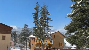 Un albergue cubierto de nieve con cabañas de madera, una terraza de madera y un paisaje de montañas al fondo.