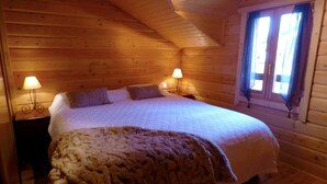 Un dormitorio rústico de madera con cama, dos lámparas de noche y una ventana con cortinas.