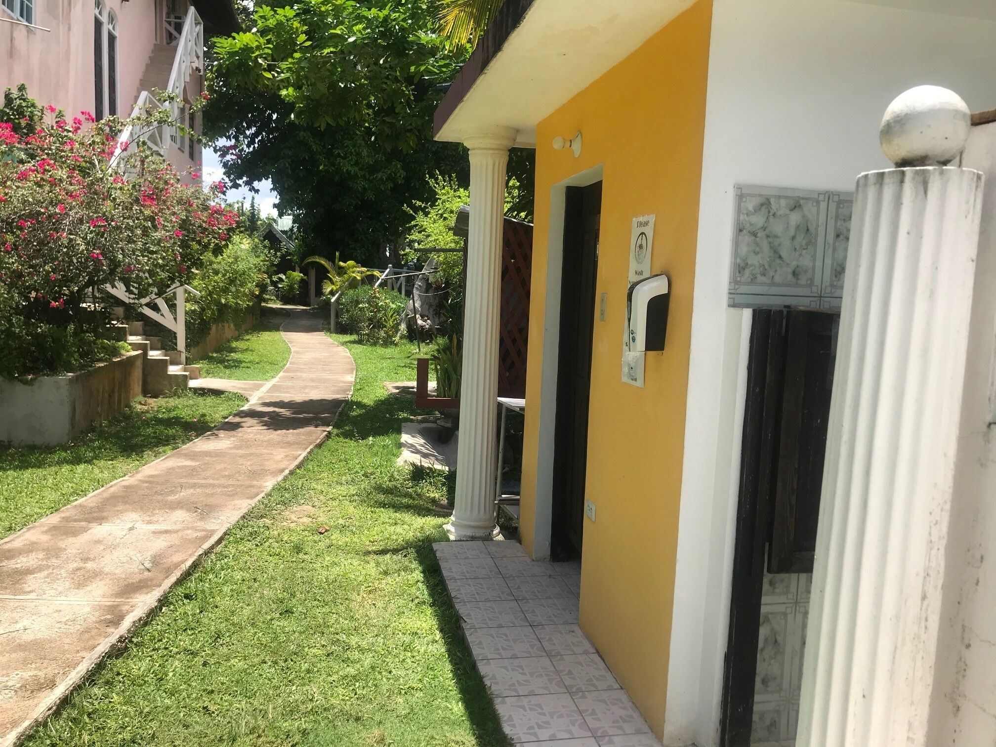 A pathway leading to a building with a yellow facade and white columns.