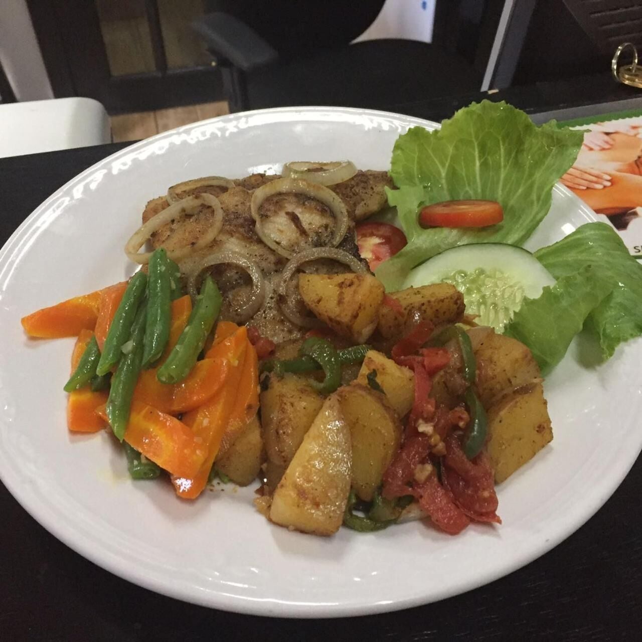 Un plato de comida con carne a la parrilla, cebollas, papas, judías verdes, zanahorias y una ensalada.