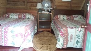 A cozy room with two beds, a wooden ceiling, a small fan, and a woven rug. - Secret Cabins at Firefly Beach (Negril)