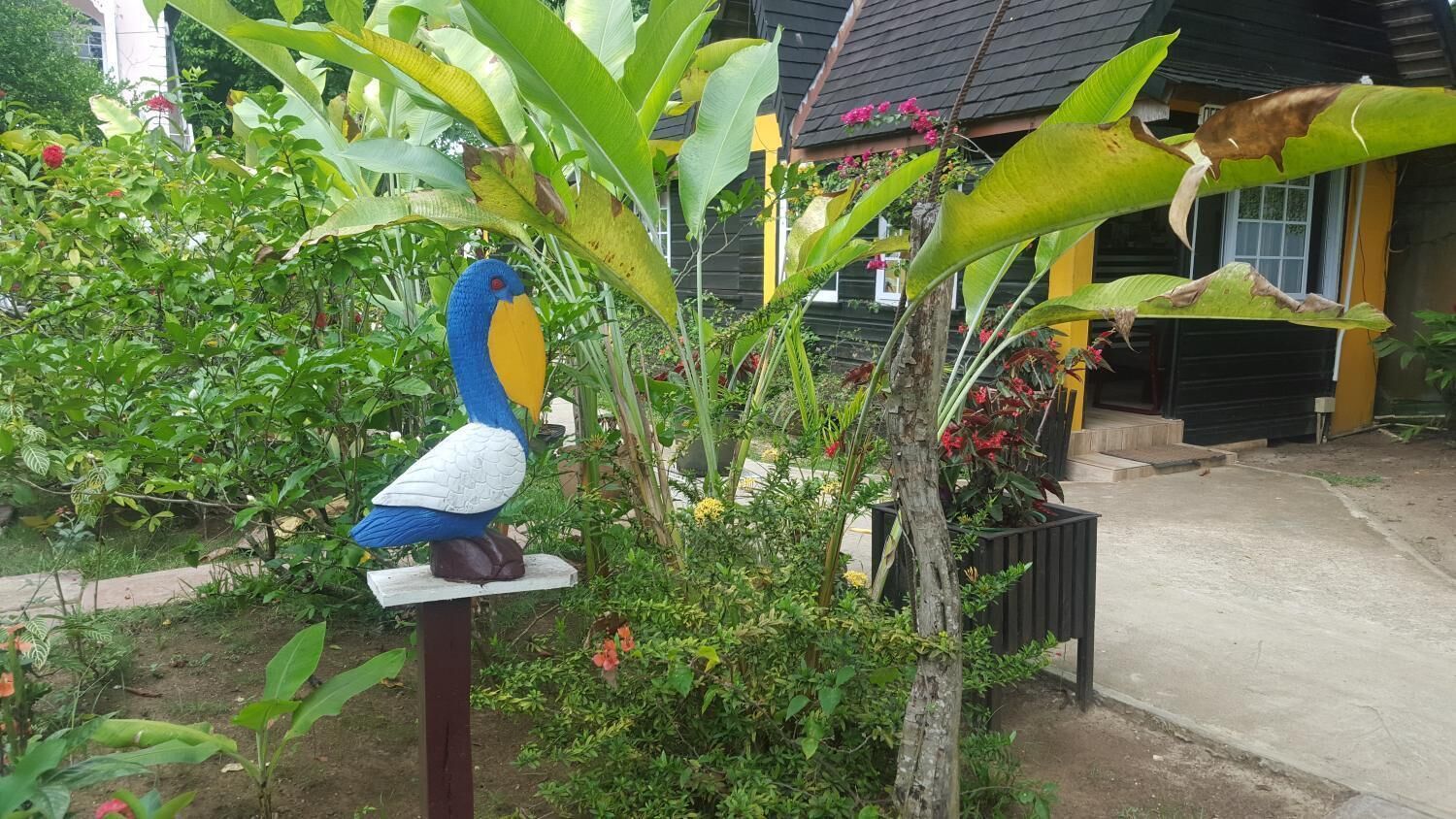A bird sculpture on a pedestal in a garden with various plants and a house in the background.