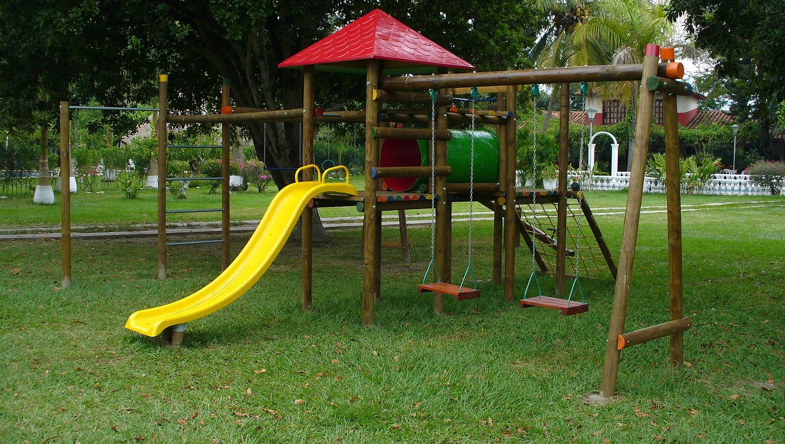 A playground with a yellow slide, swings, and a red-roofed climbing structure.