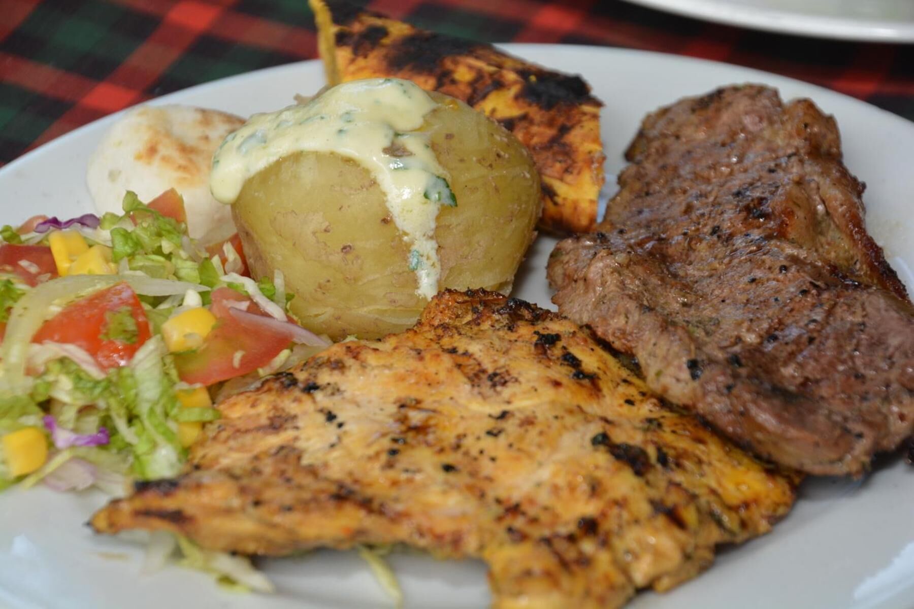 Un plat amb carn a la planxa, una patata a la planxa, una amanida i un tros de pollastre a la planxa.