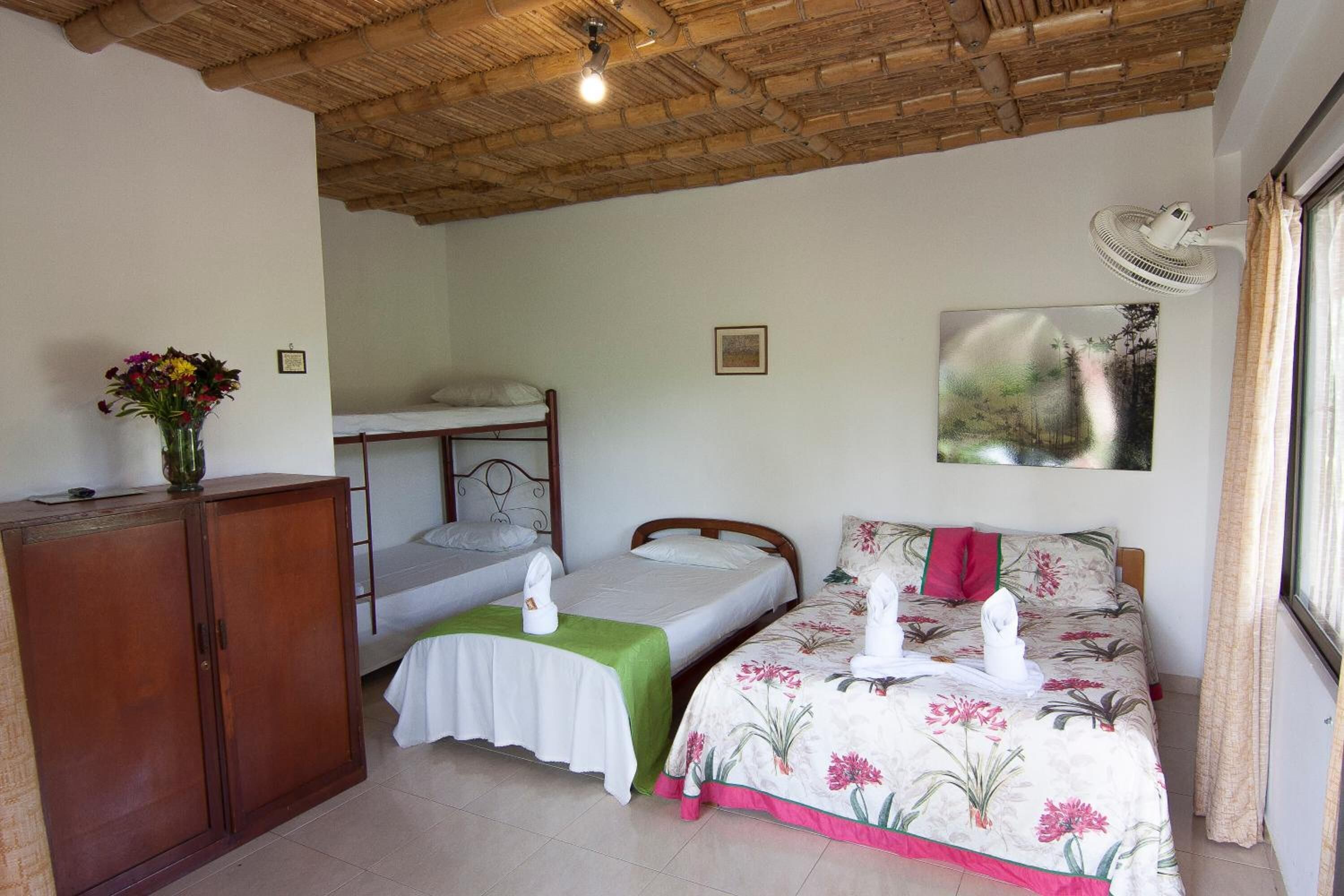 A room with a bunk bed, a single bed with floral bedding, a wooden cabinet, and a painting on the wall.