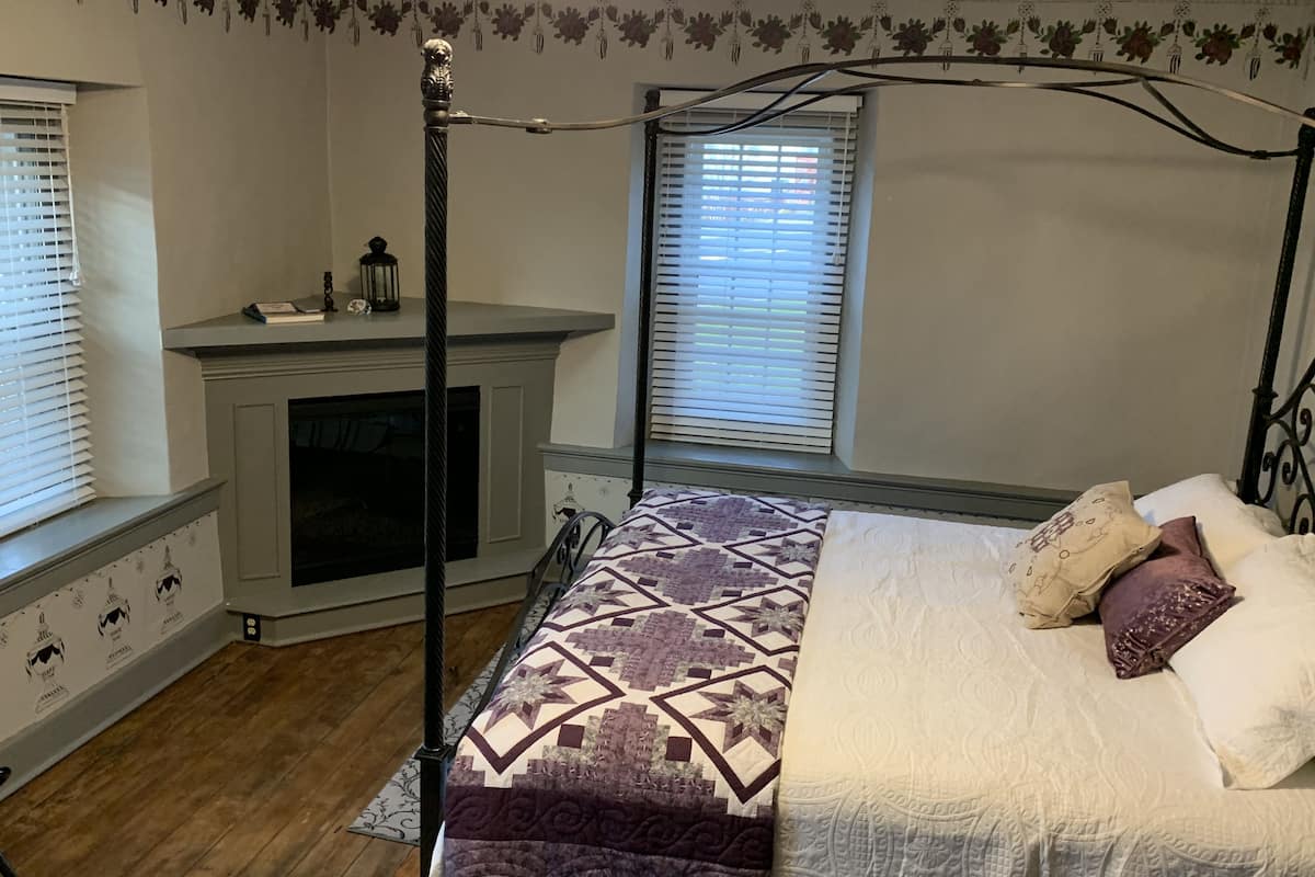 A bedroom with a four-poster bed, a fireplace, and a window with blinds.