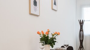 Un coin repas avec une table dressée pour deux personnes, un vase rempli de fleurs et deux tableaux encadrés accrochés au mur.